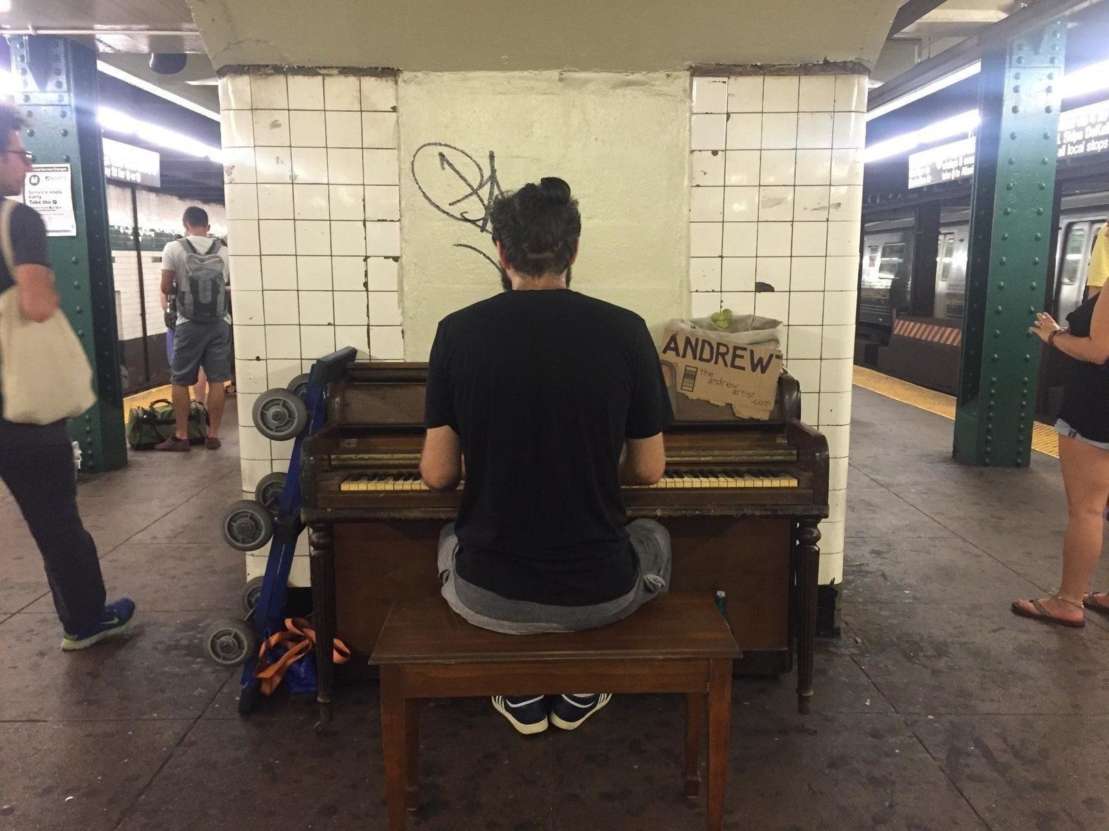 A man sitting on a subway platform playing an upright piano