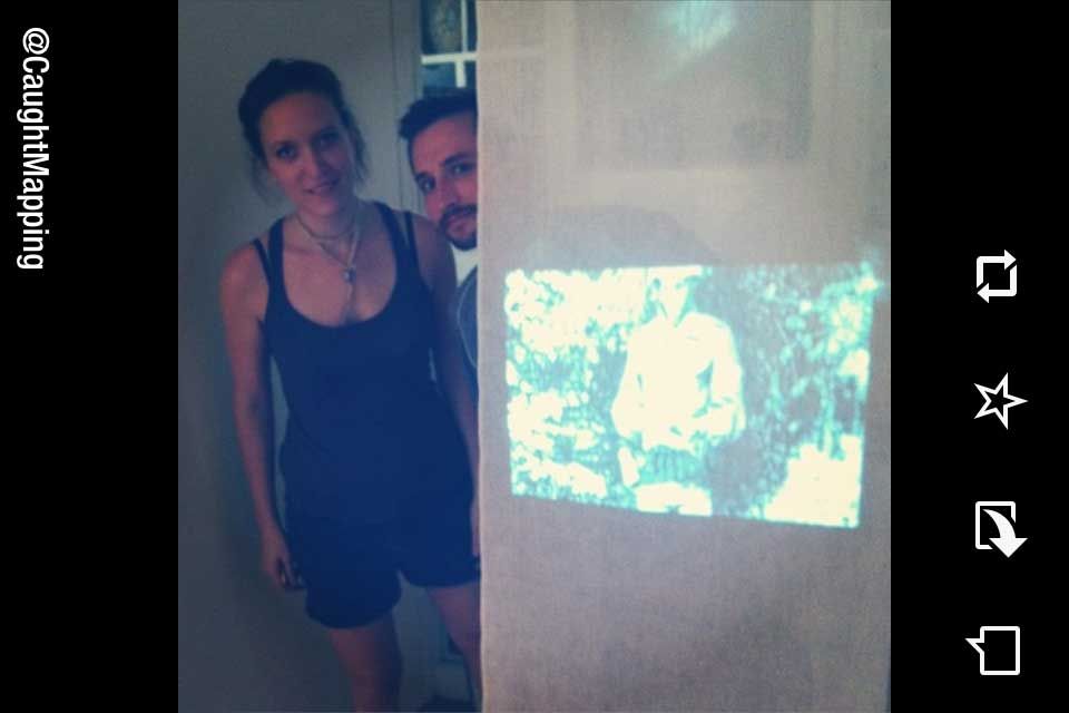 Two people posing for a photo behind a projected video display of a map