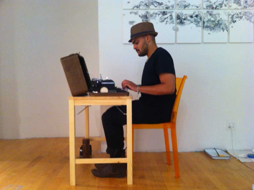 A man sitting at a small desk with a typewriter